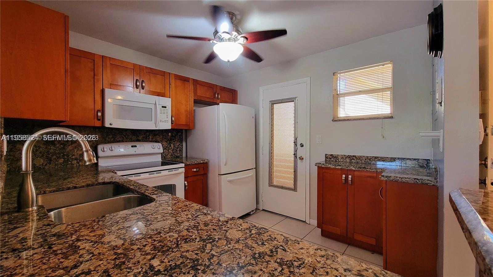 A kitchen features wood cabinets, granite countertops, white appliances, and a ceiling fan — 406 NW 68th Ave # 304, Plantation FL 33317, PLANTATION, FL