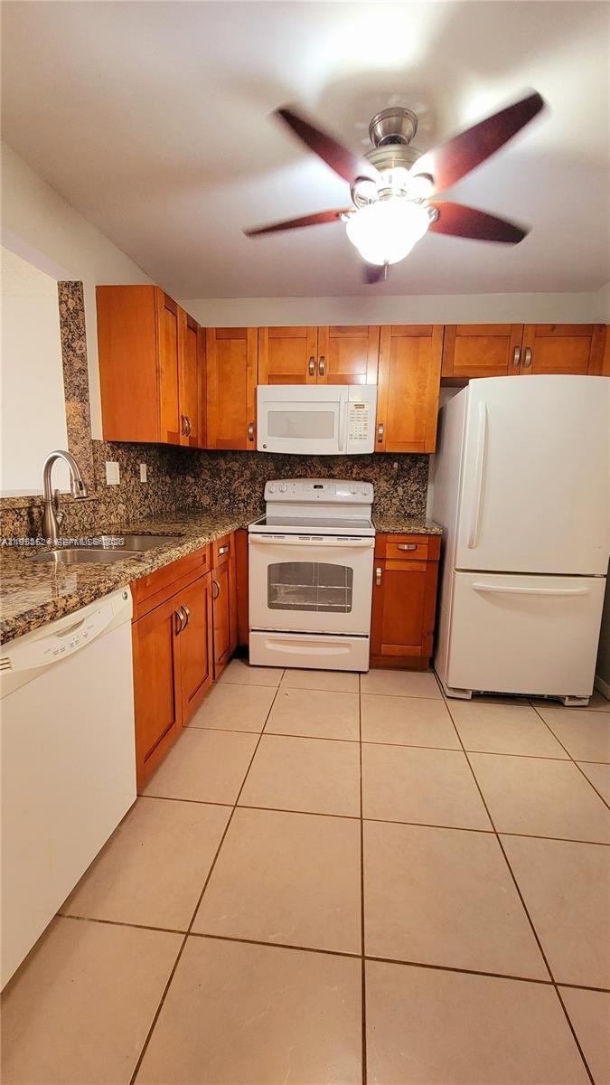 A kitchen with wood cabinets, granite countertops, white appliances, and light-colored tile flooring — 406 NW 68th Ave # 304, Plantation FL 33317, PLANTATION, FL