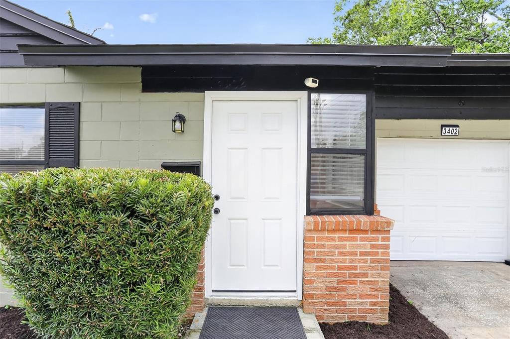 The exterior of a house features a white front door, brick accents, and a bush — 3402 LEWIS COURT, ORLANDO, FL