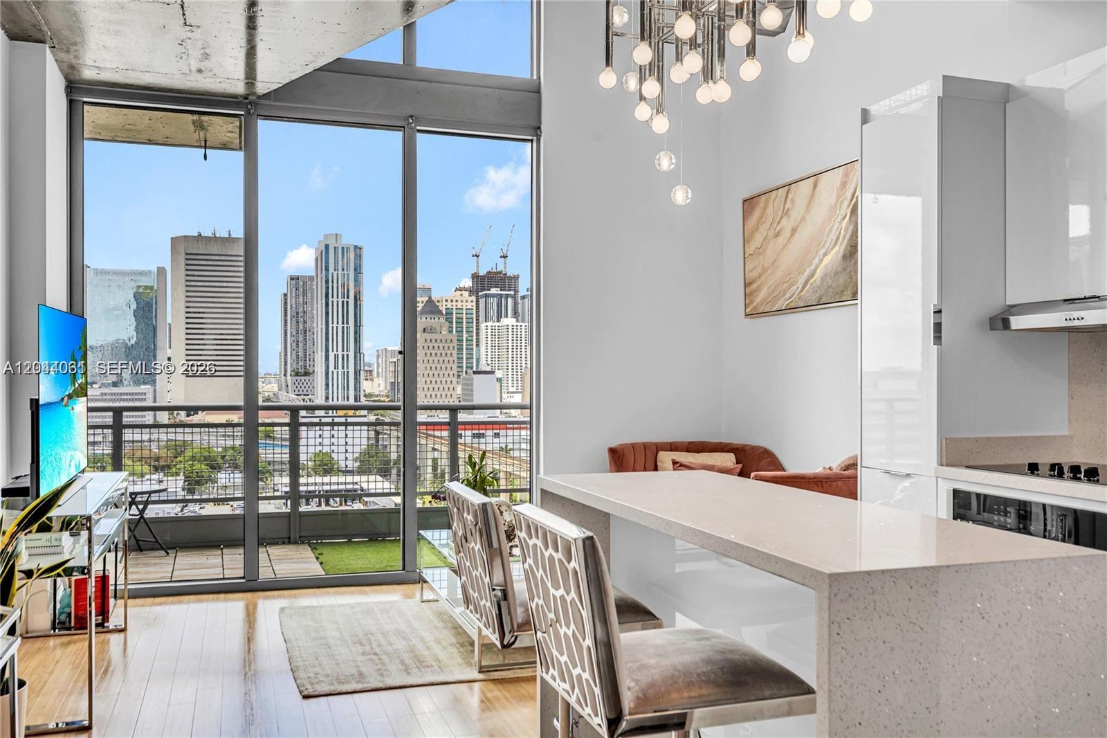 A modern kitchen with a quartz island and bar stools overlooks a city skyline view — 690 SW 1st Ct # 1709, Miami FL 33130, MIAMI, FL