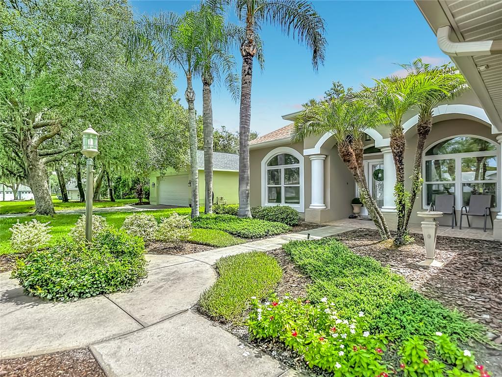 A concrete walkway leads to the front entrance of a house with palm trees — 13540 PLANTATION LAKE CIRCLE, HUDSON, FL