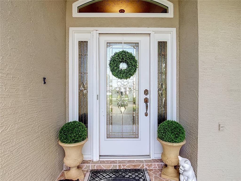 A white front door with glass panels and sidelights is flanked by two potted topiaries — 13540 PLANTATION LAKE CIRCLE, HUDSON, FL
