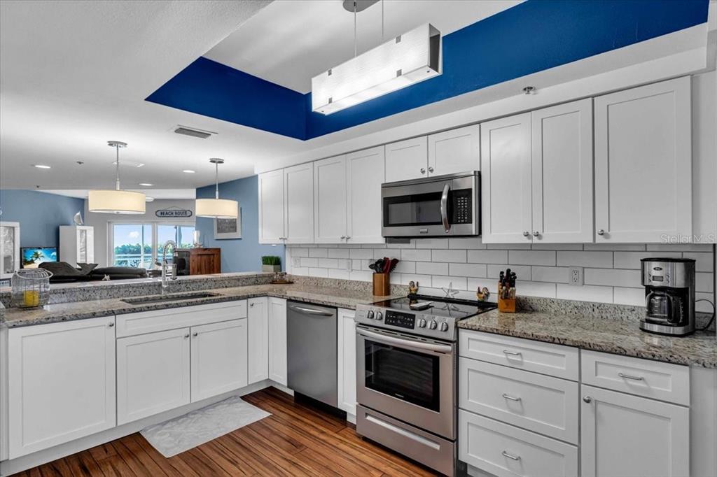 A kitchen features white cabinetry, granite countertops, stainless steel appliances, and a blue tray ceiling — 5621 GULF OF MEXICO DRIVE UNIT 102, LONGBOAT KEY, FL