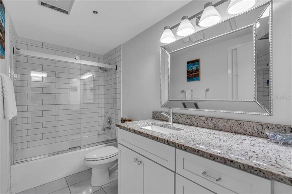 A bathroom features a white vanity with a granite countertop, a mirror, and a tiled shower — 5621 GULF OF MEXICO DRIVE UNIT 102, LONGBOAT KEY, FL