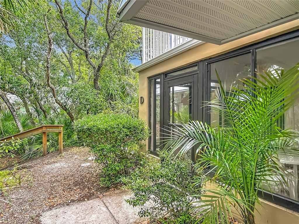 An exterior view of a building entrance with a screened door, landscaping, and wooden stairs — 4150 S ATLANTIC AVENUE UNIT 113D, NEW SMYRNA BEACH, FL