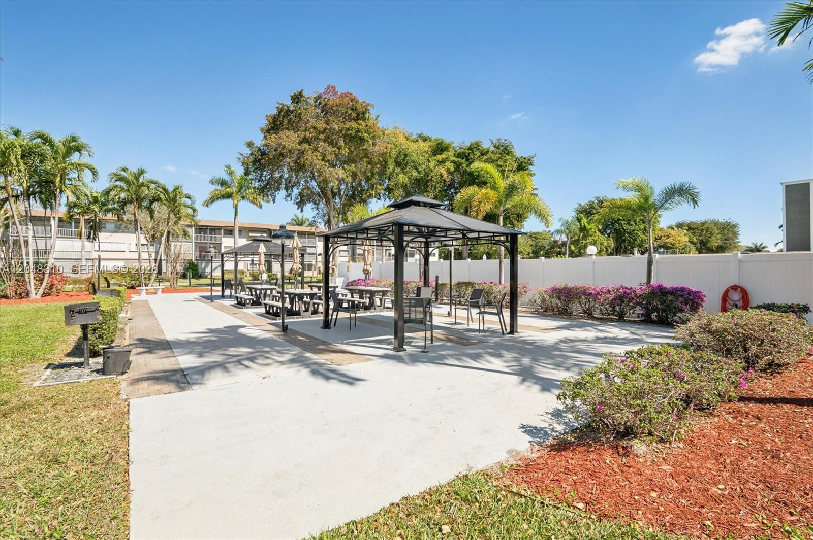 A paved outdoor patio features two metal gazebos with tables and chairs near a white fence — 1000 Hillcrest Ct # 303, Hollywood FL 33021, HOLLYWOOD, FL