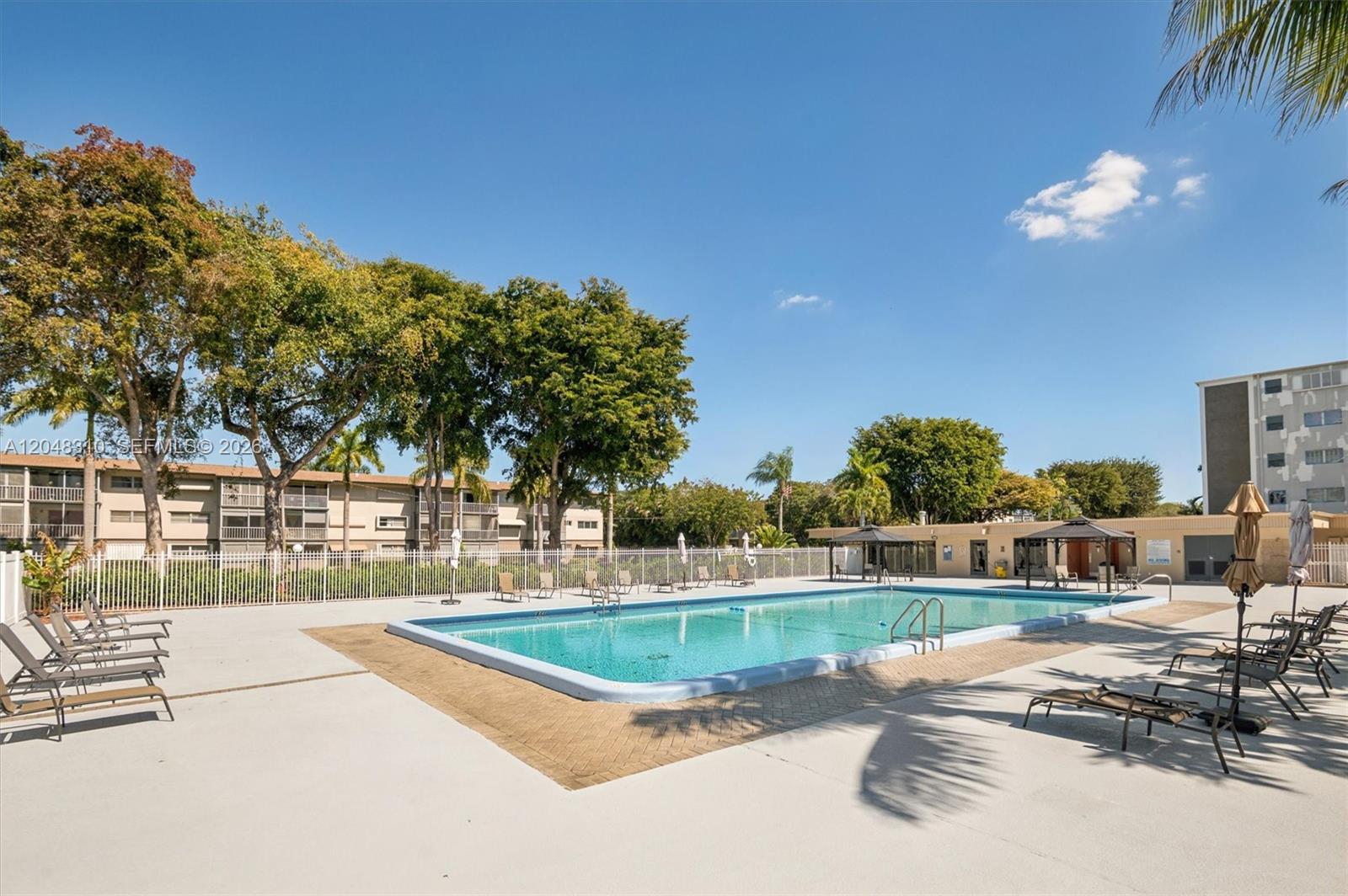 An outdoor swimming pool is surrounded by a concrete deck, lounge chairs, and apartment buildings — 1000 Hillcrest Ct # 303, Hollywood FL 33021, HOLLYWOOD, FL
