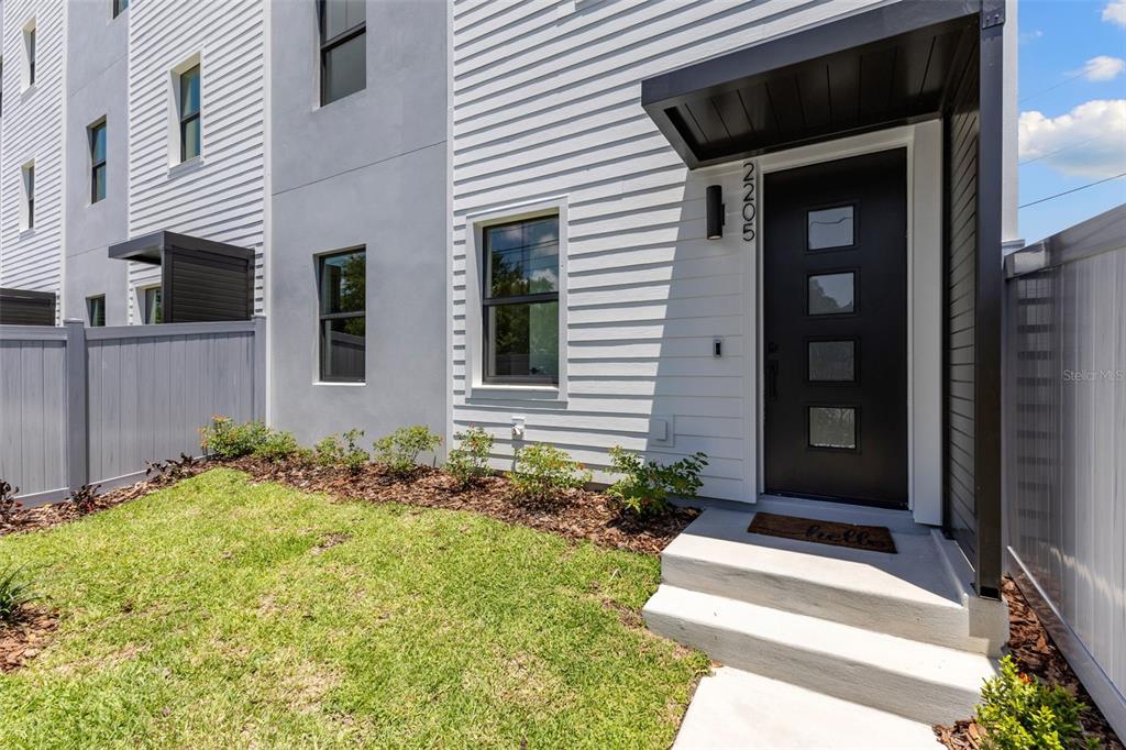 A modern townhouse entrance features white siding, a black door with windows, and concrete steps — 2205 16TH STREET N, ST PETERSBURG, FL