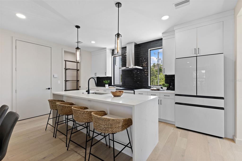 A modern kitchen features white cabinetry, a marble-topped island with woven stools, and black tile — 2205 16TH STREET N, ST PETERSBURG, FL