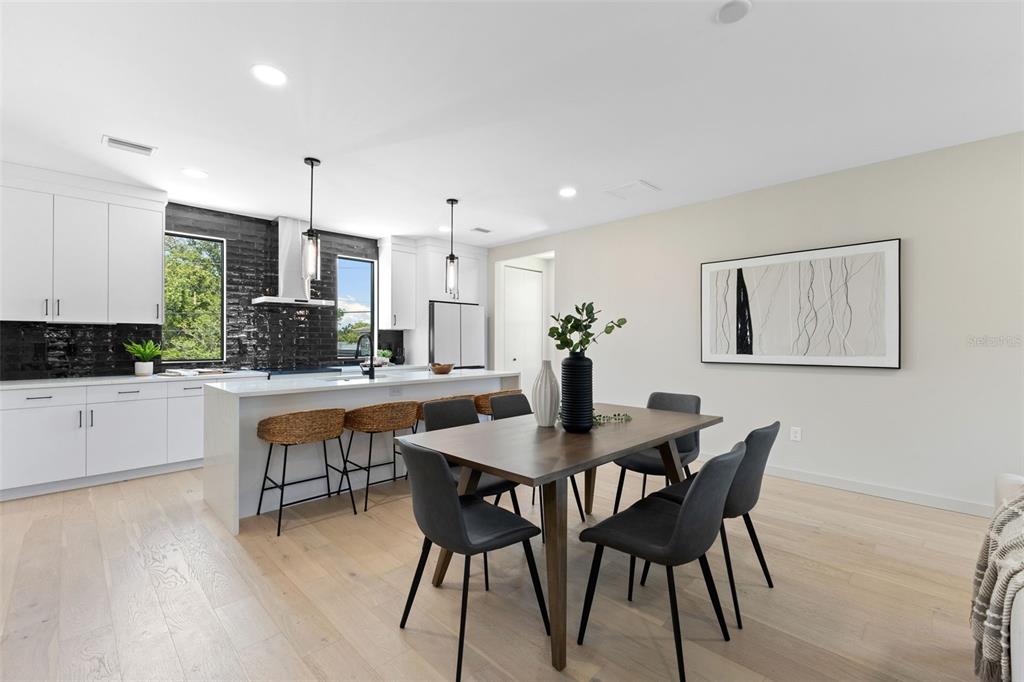 A modern kitchen and dining area feature white cabinetry, a black tile backsplash, and wood flooring — 2205 16TH STREET N, ST PETERSBURG, FL