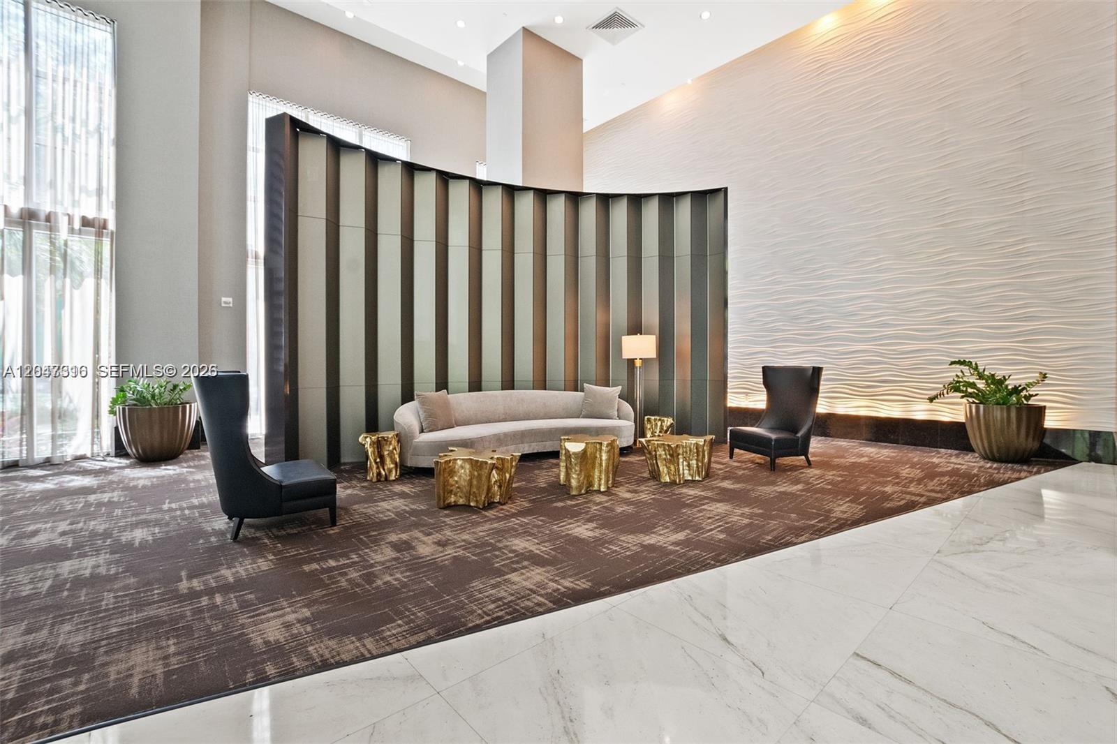 A modern lobby features a curved screen, a sofa, gold accent tables, and textured walls — 951 Brickell Ave # 3207, Miami FL 33131, MIAMI, FL