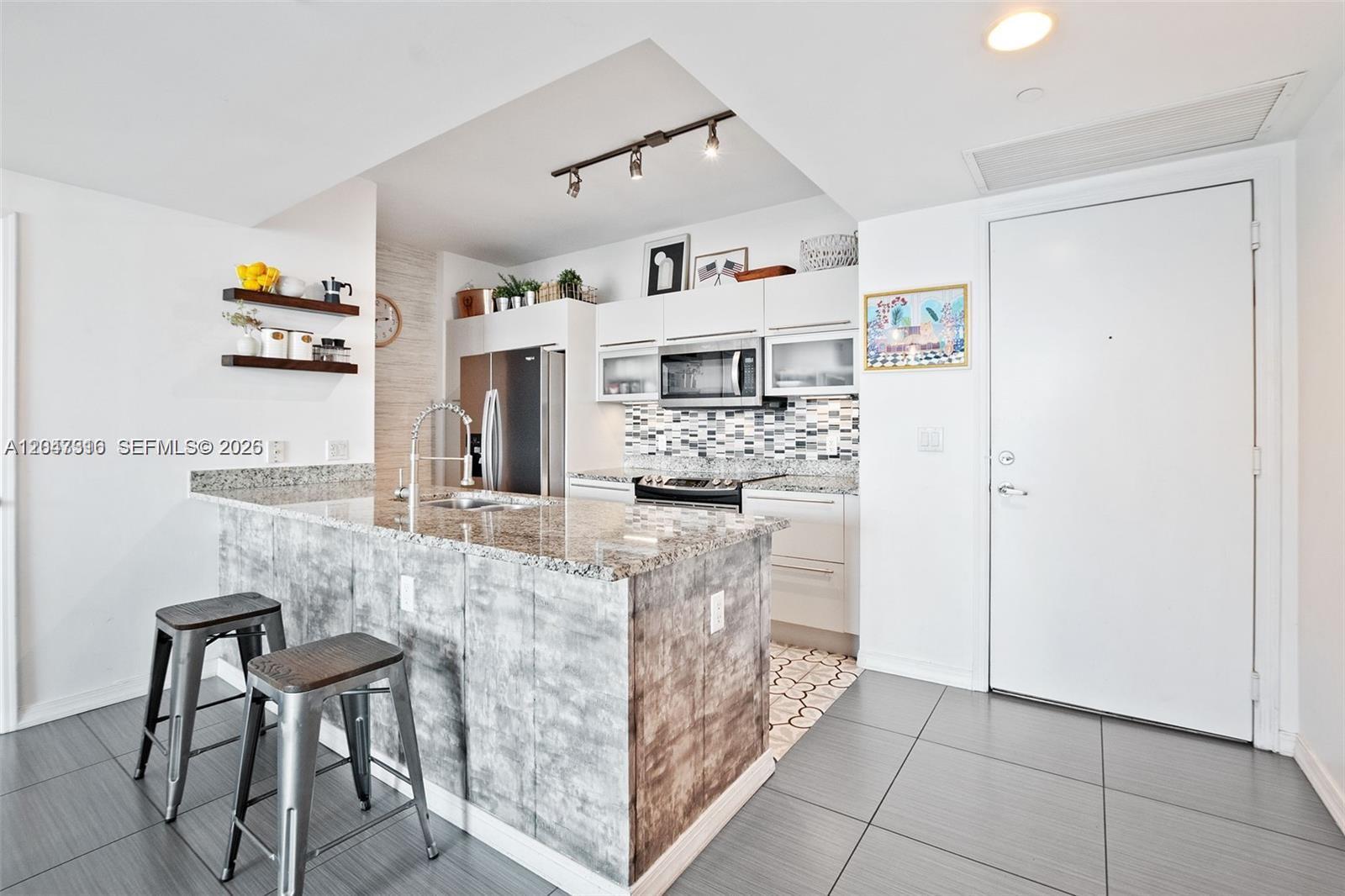 A modern kitchen features a granite-topped island, stainless steel appliances, and gray tile flooring — 951 Brickell Ave # 3207, Miami FL 33131, MIAMI, FL