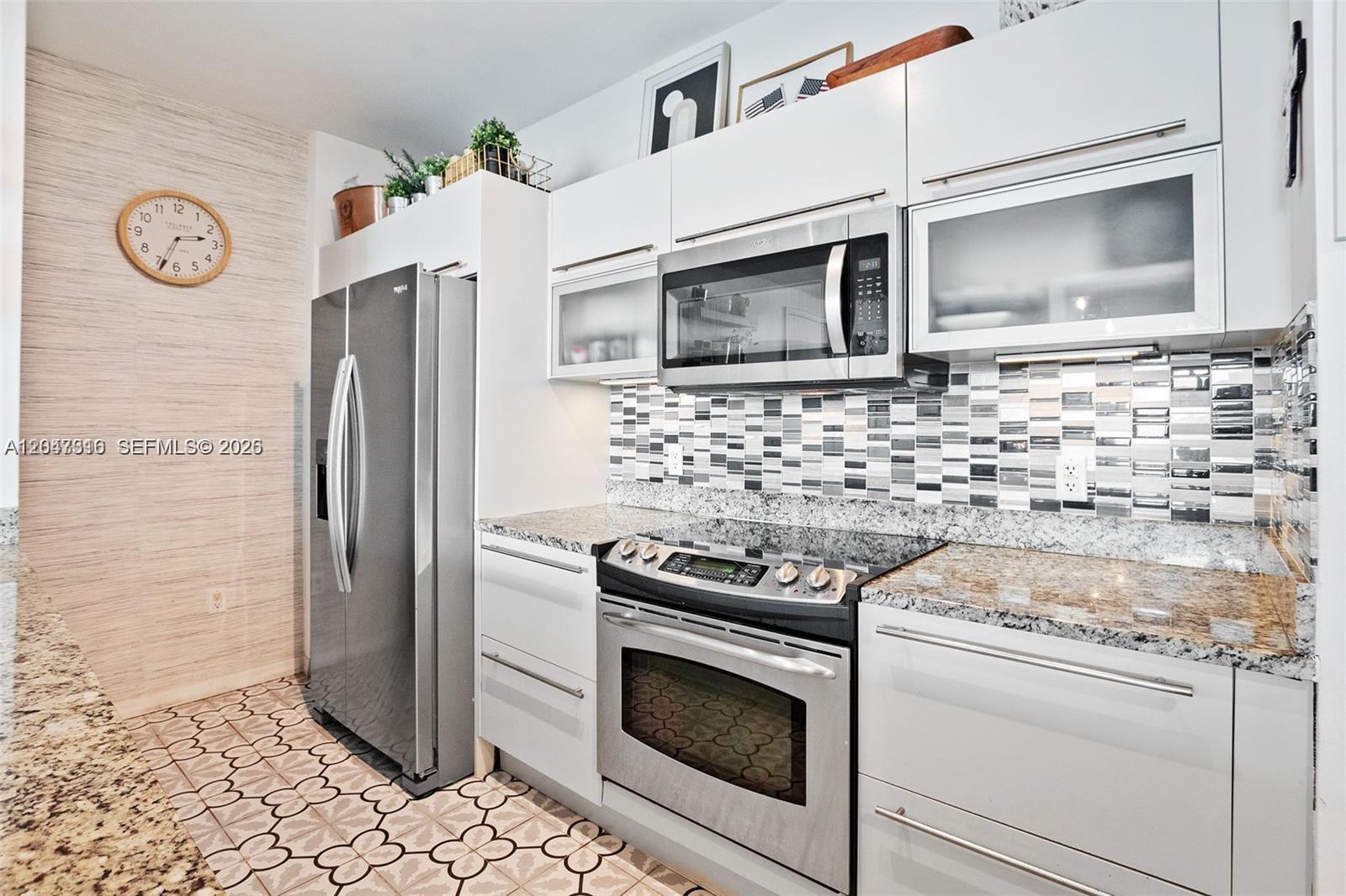 A modern kitchen features stainless steel appliances, white cabinetry, granite countertops, and patterned floor tiles — 951 Brickell Ave # 3207, Miami FL 33131, MIAMI, FL