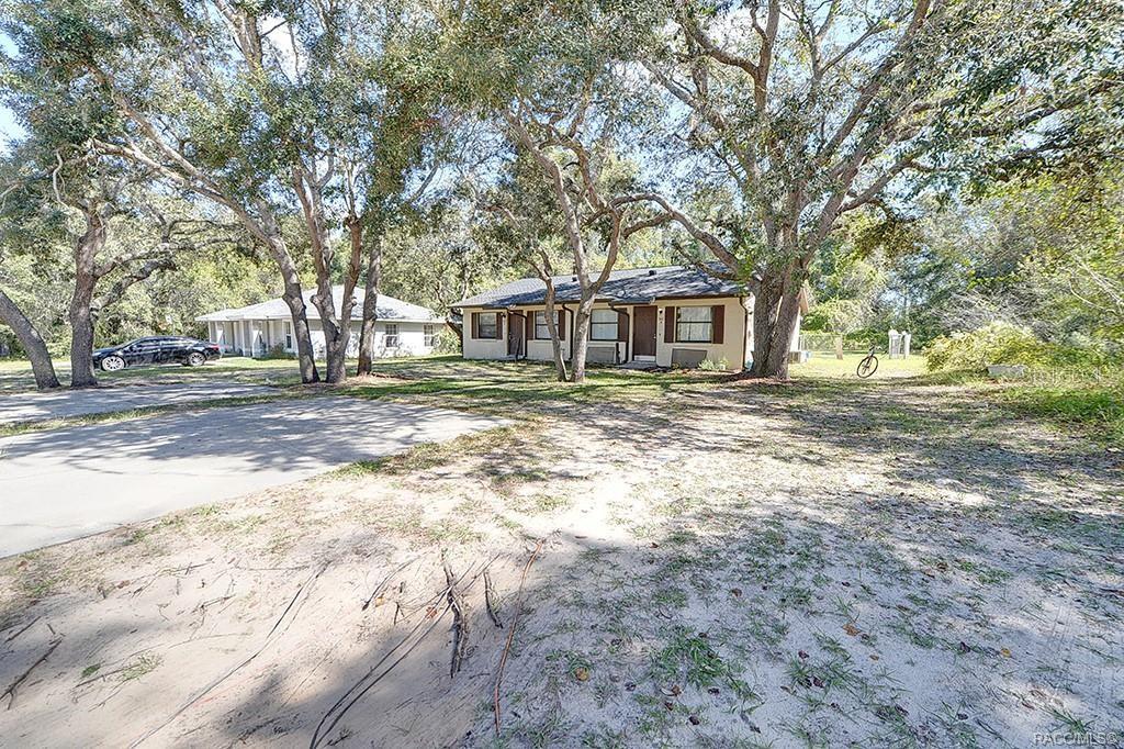 A single-story house with a tan exterior sits on a sandy lot among many trees — 512 LONG AVENUE, INVERNESS, FL