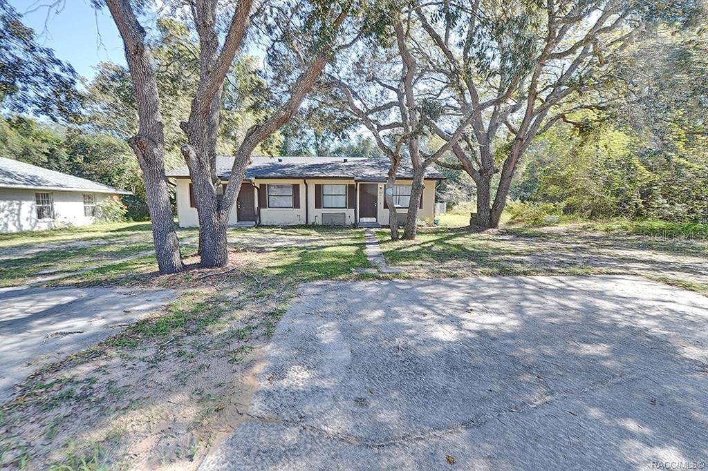 A single-story duplex with a concrete driveway and large trees in the front yard — 512 LONG AVENUE, INVERNESS, FL