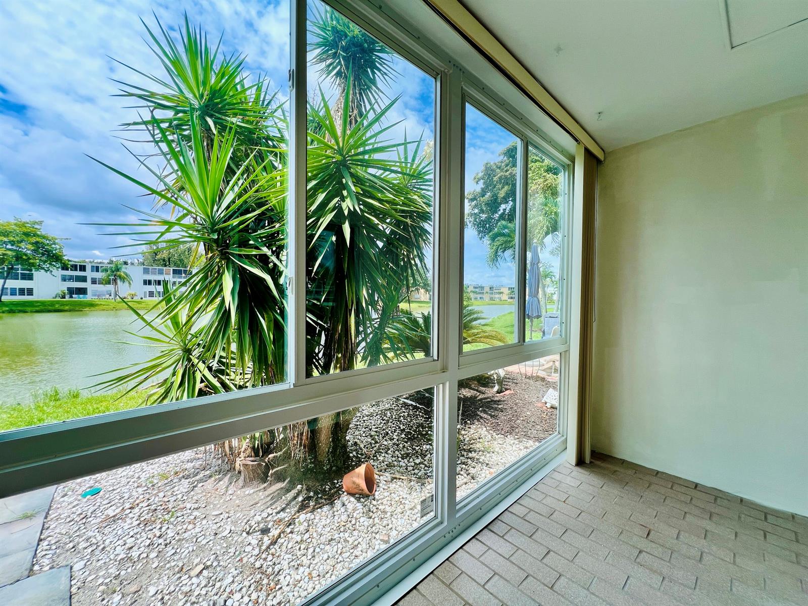 A sunroom with tiled flooring and large windows overlooking a lake and palm trees — 107 Wellington D, West Palm Beach FL 33417, WEST PALM BEACH, FL