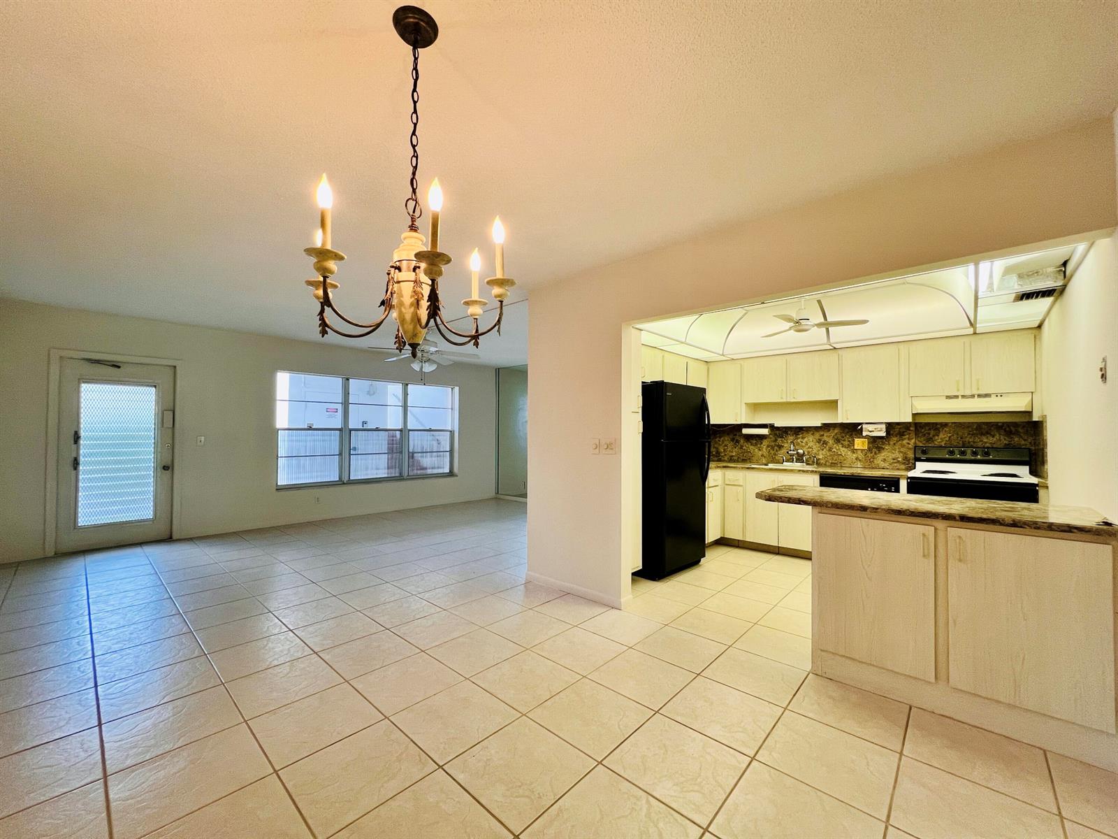 A tiled dining area with a chandelier opens to a kitchen featuring light-colored cabinetry — 107 Wellington D, West Palm Beach FL 33417, WEST PALM BEACH, FL