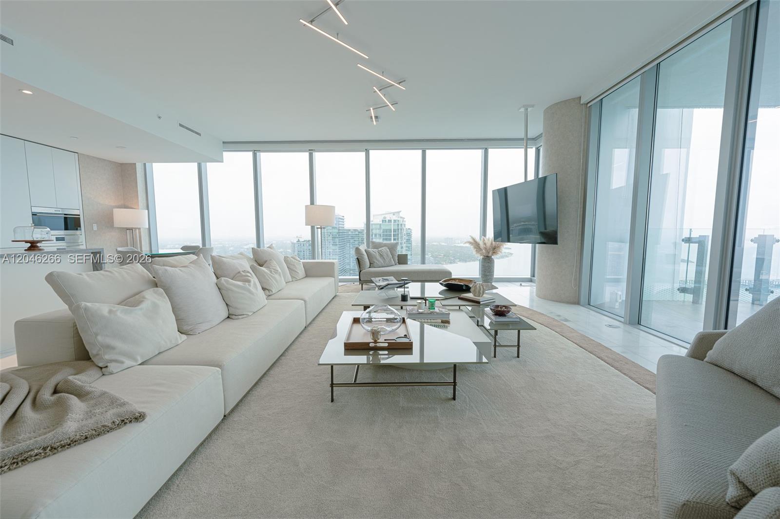 A modern living room features a large white sectional sofa, glass coffee tables, and floor-to-ceiling windows — 700 NE 26th Ter # 4901, Miami FL 33137, MIAMI, FL