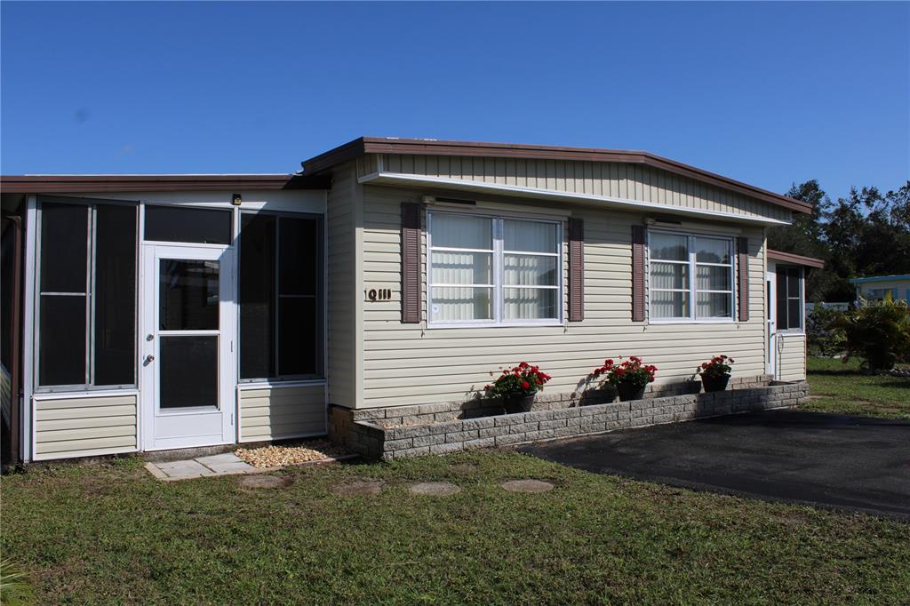A single-story manufactured home with light siding, a screened-in porch, and a stone planter box — 5316 53RD AVENUE E UNIT Q111, BRADENTON, FL