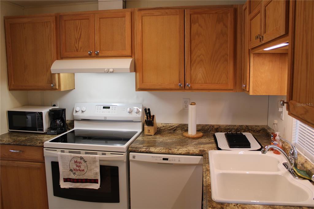 A kitchen features wood cabinets, granite countertops, a white stove, and a double-basin sink — 5316 53RD AVENUE E UNIT Q111, BRADENTON, FL