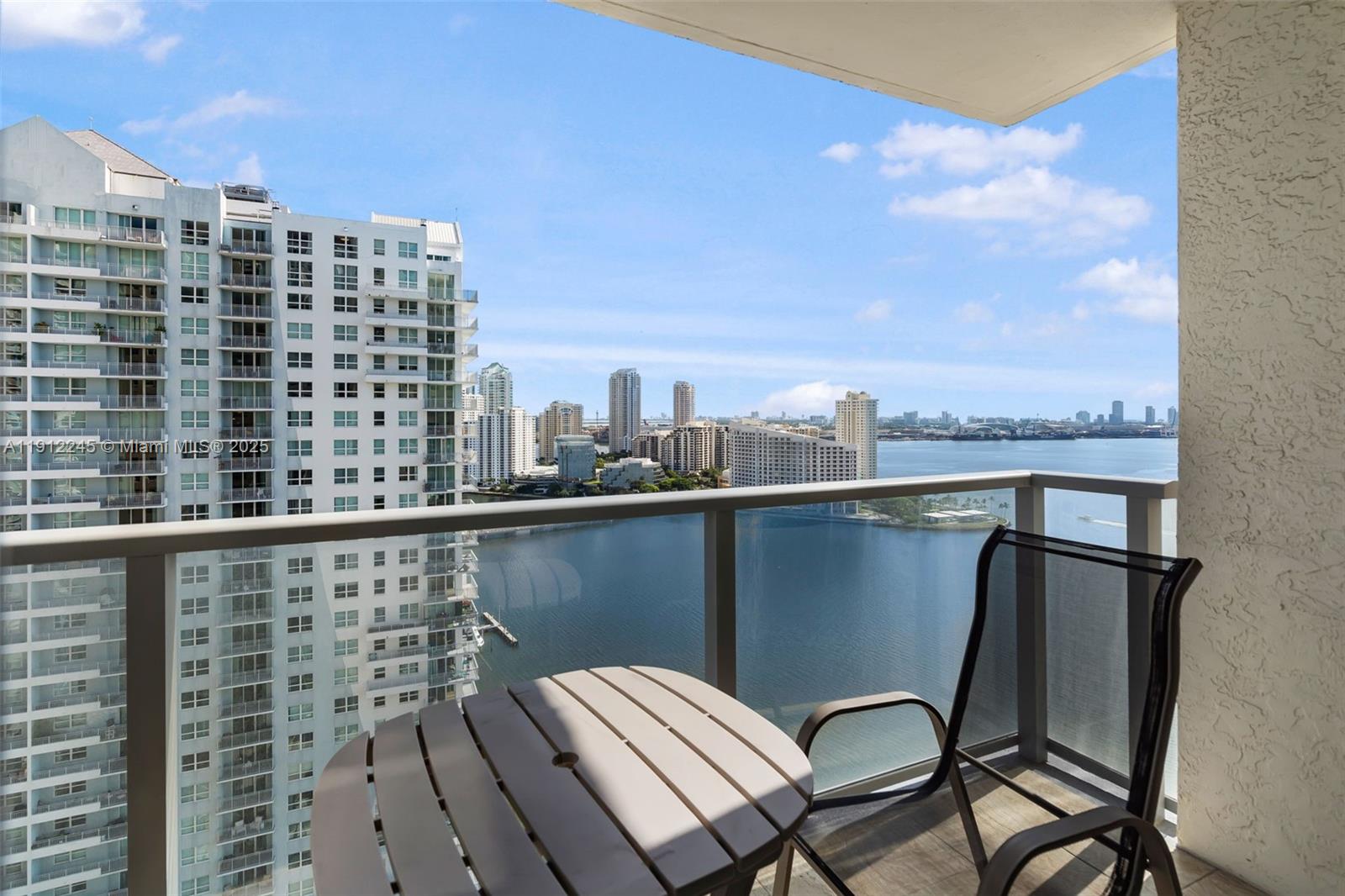 A balcony with a small table and chair overlooks a bay and city skyline — 1155 BRICKELL BAY DR # 2708, Miami FL 33131, MIAMI, FL