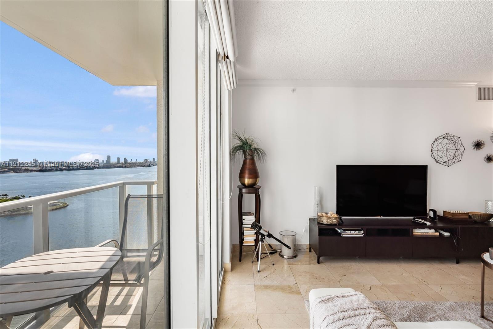 A living room with a television console, telescope, and a balcony overlooking the water — 1155 BRICKELL BAY DR # 2708, Miami FL 33131, MIAMI, FL