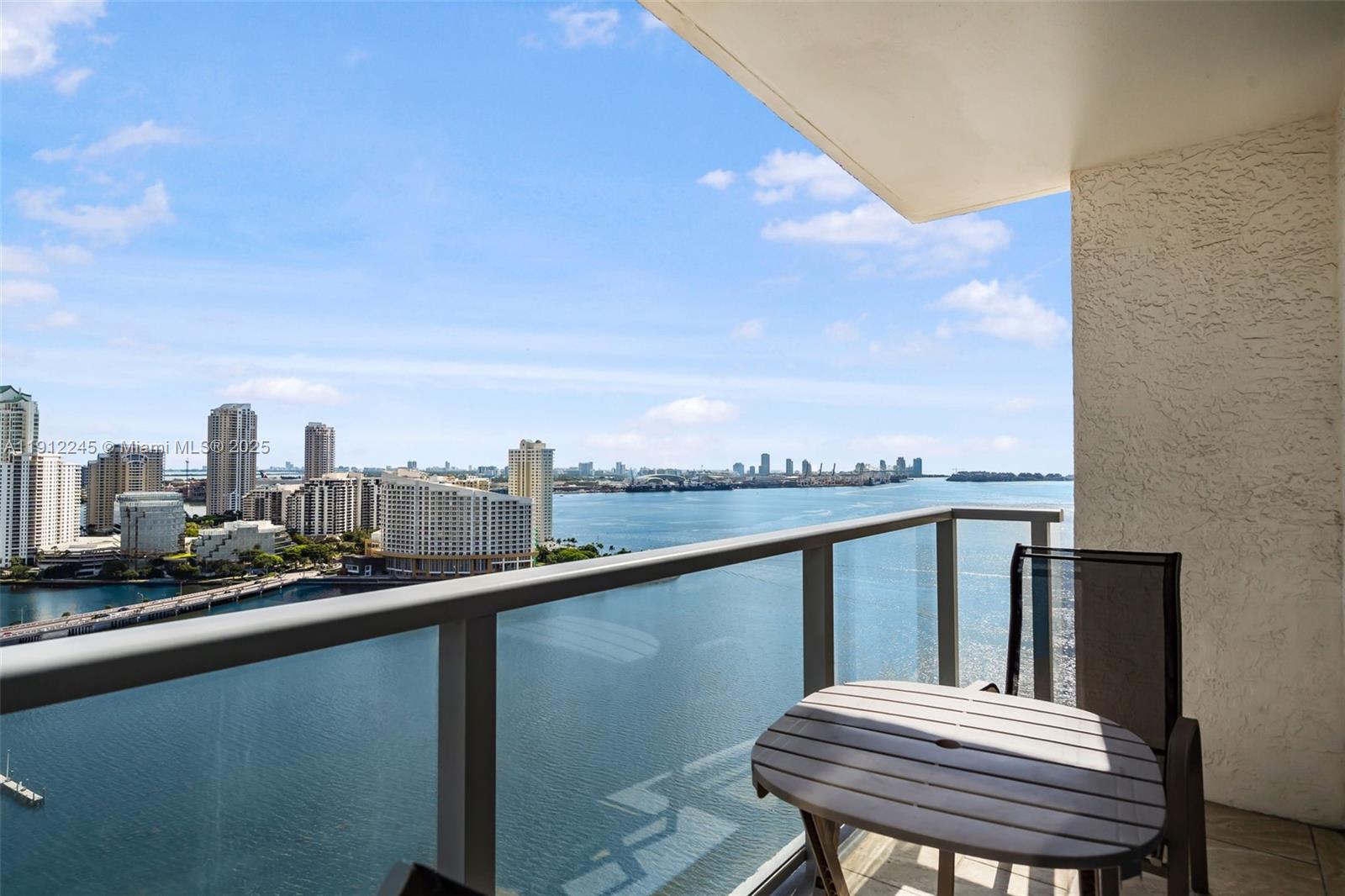 A balcony with a small table and chair overlooks a bay and city skyline — 1155 BRICKELL BAY DR # 2708, Miami FL 33131, MIAMI, FL