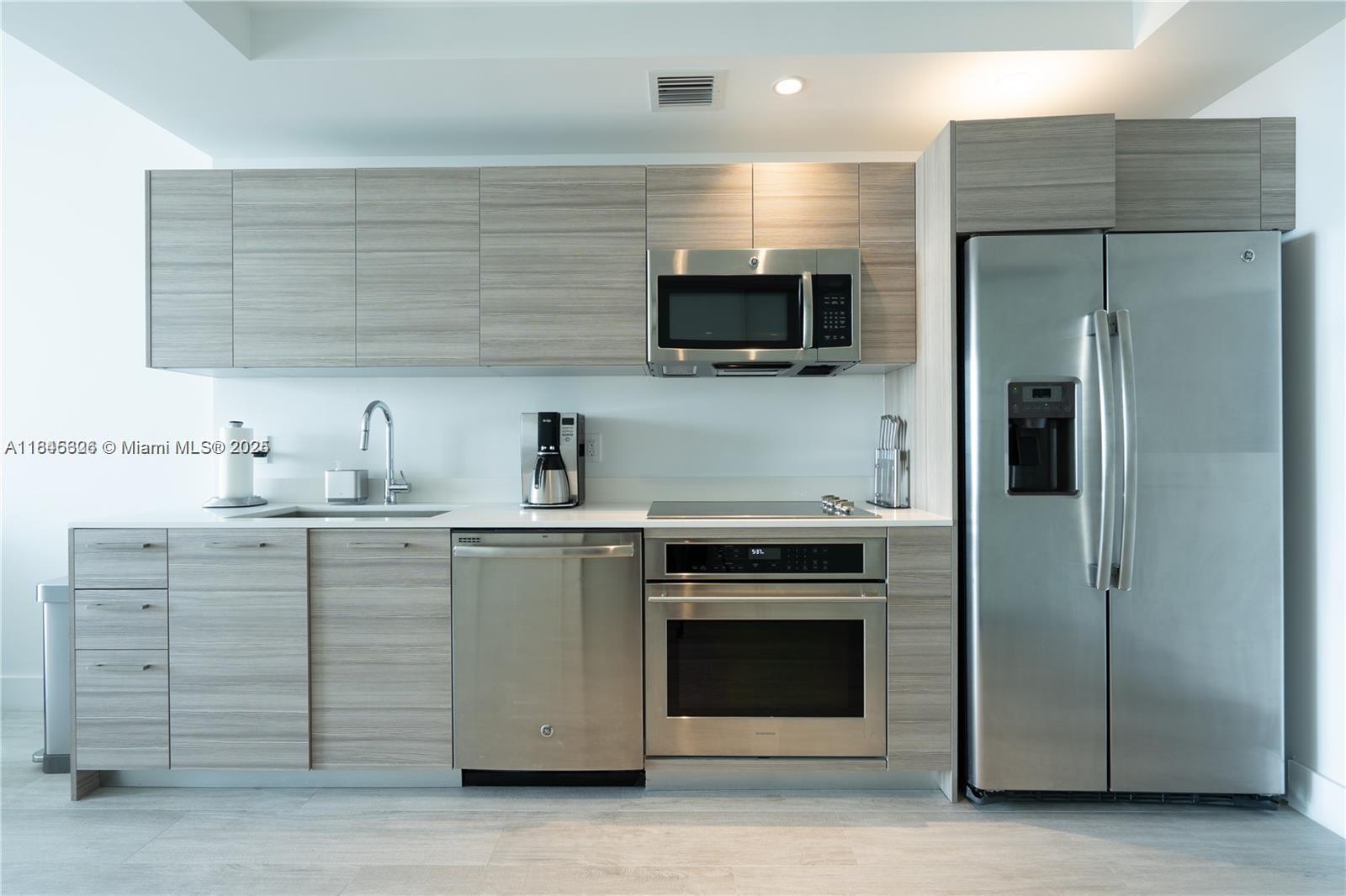 A modern kitchen features light wood-grain cabinetry, stainless steel appliances, and a white countertop — 121 NE 34th St # 806, Miami FL 33137, MIAMI, FL