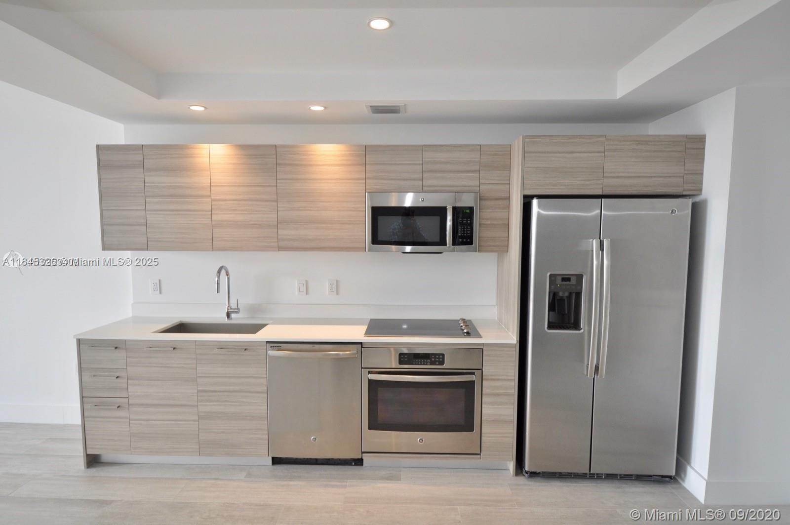 A modern kitchen features light wood cabinetry, stainless steel appliances, and white countertops — 121 NE 34th St # 806, Miami FL 33137, MIAMI, FL