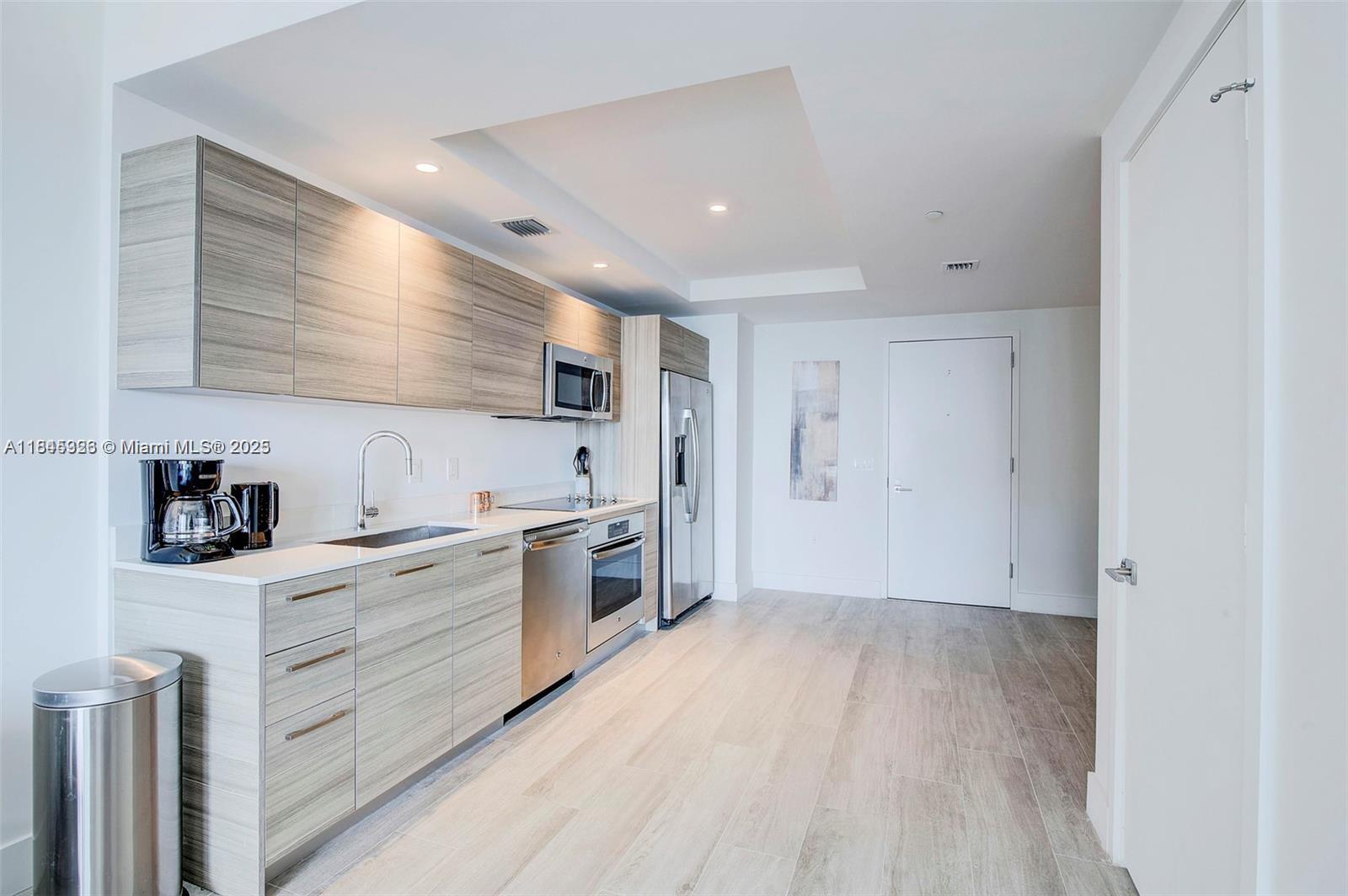 A modern kitchen features light wood cabinetry, stainless steel appliances, and light-toned flooring — 121 NE 34th St # 806, Miami FL 33137, MIAMI, FL