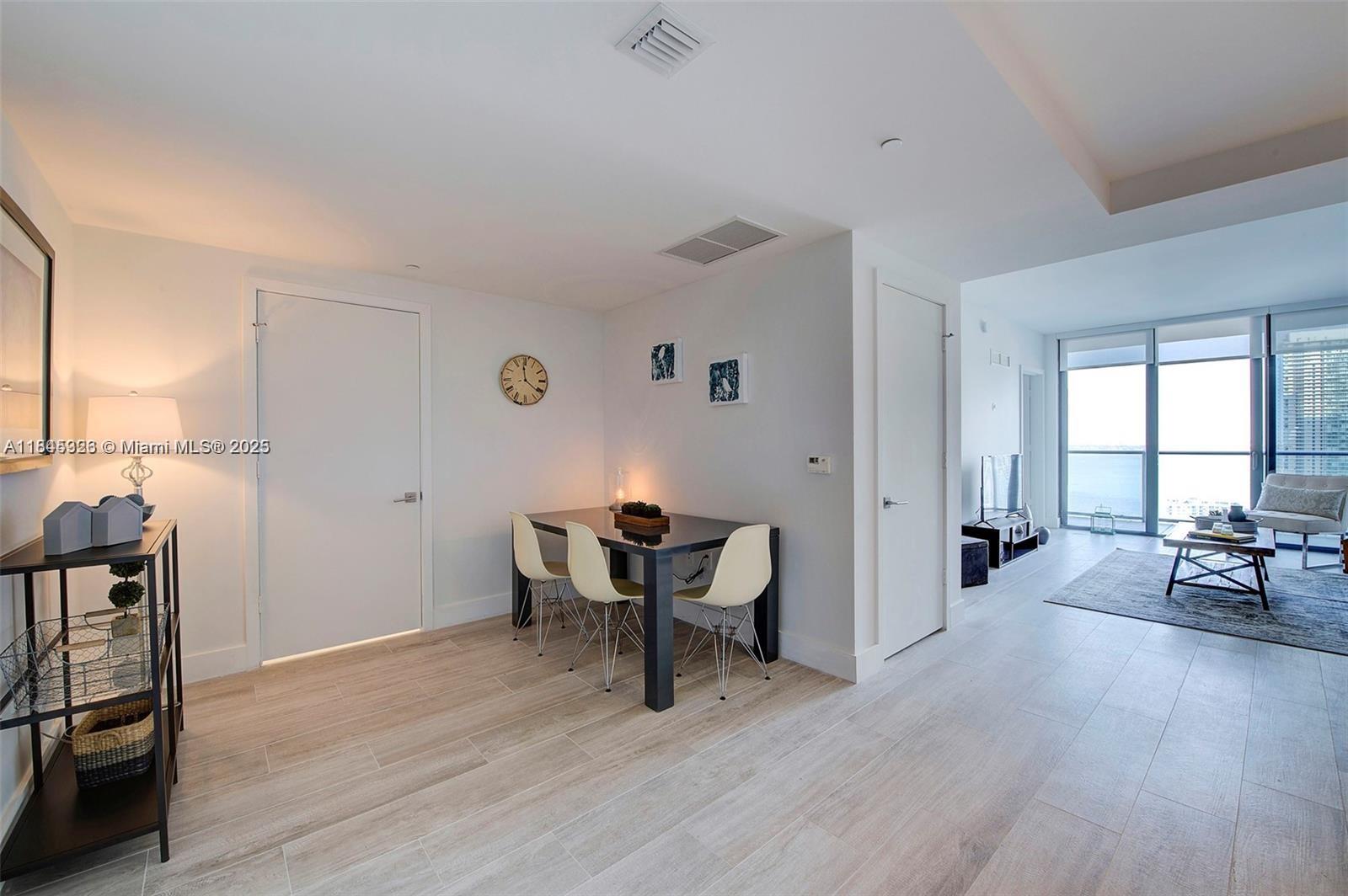 A dining area with a dark table and white chairs sits next to a living room — 121 NE 34th St # 806, Miami FL 33137, MIAMI, FL