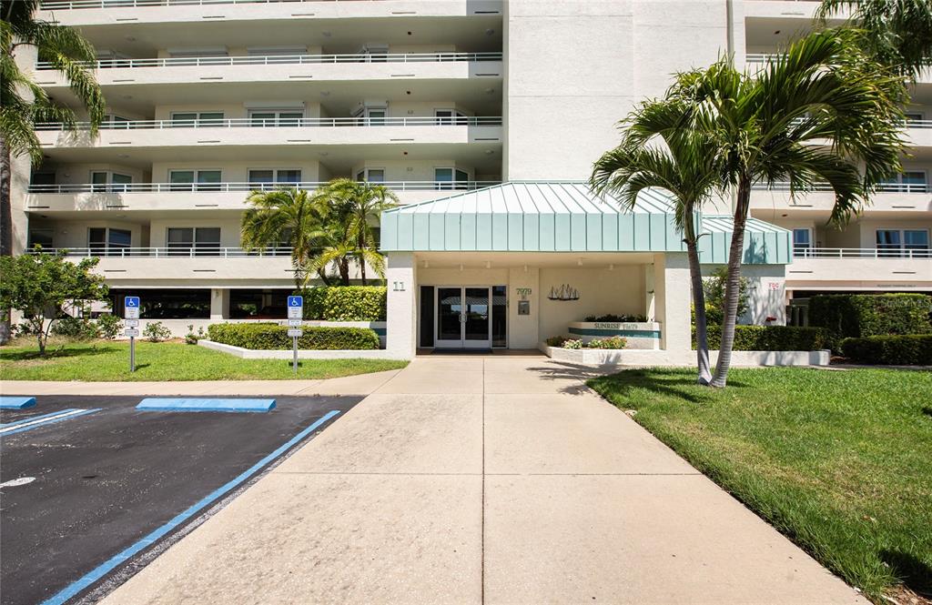 The exterior of a multi-story apartment building features a covered entrance and palm trees — 7979 SAILBOAT KEY BOULEVARD S UNIT 208, SOUTH PASADENA, FL