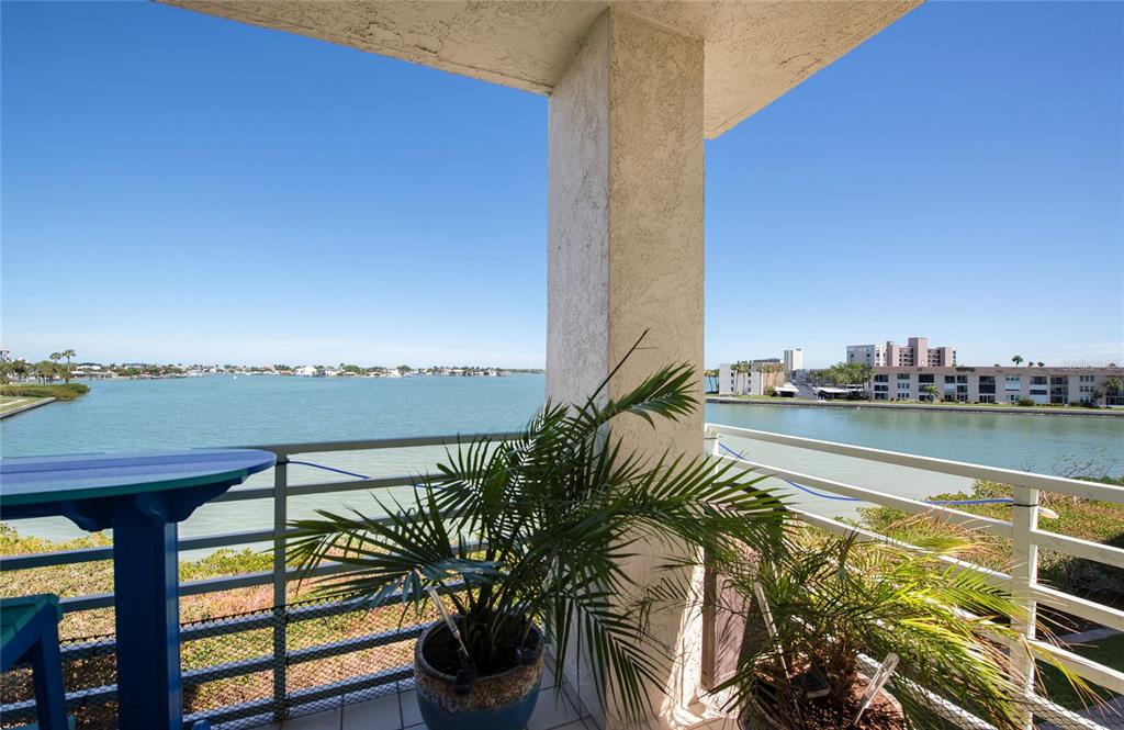 A balcony with a potted palm tree overlooks a wide bay with distant buildings — 7979 SAILBOAT KEY BOULEVARD S UNIT 208, SOUTH PASADENA, FL