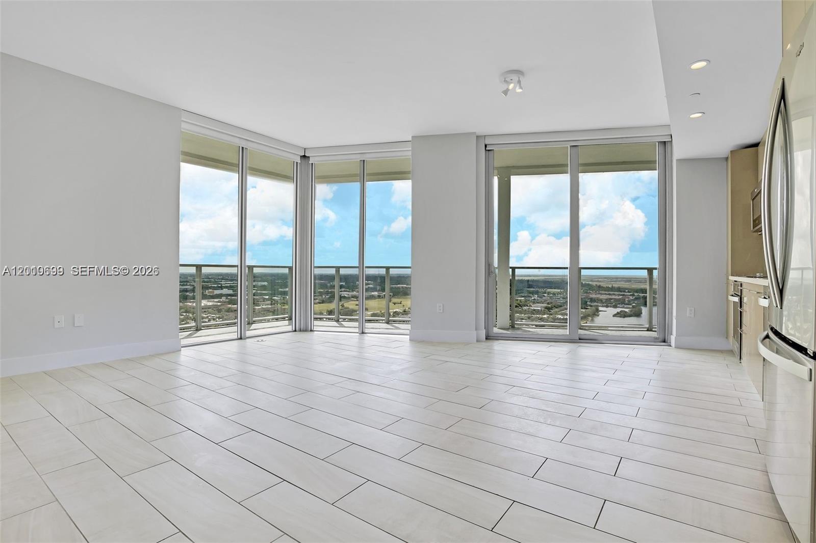 An open-concept living area features light-colored tile flooring, floor-to-ceiling windows, and a modern kitchen — 2000 Metropica Way # 2204, Sunrise FL 33323, SUNRISE, FL