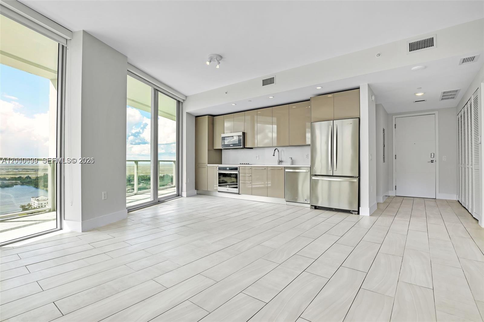 A modern kitchen with stainless steel appliances and beige cabinets opens to a balcony view — 2000 Metropica Way # 2204, Sunrise FL 33323, SUNRISE, FL