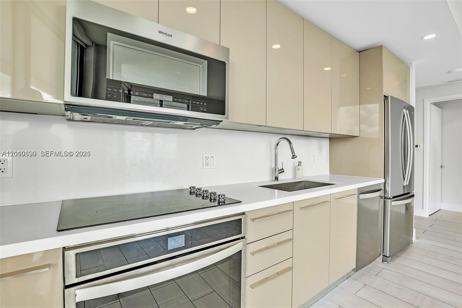 A modern kitchen features beige high-gloss cabinets, stainless steel appliances, and white countertops — 2000 Metropica Way # 2204, Sunrise FL 33323, SUNRISE, FL