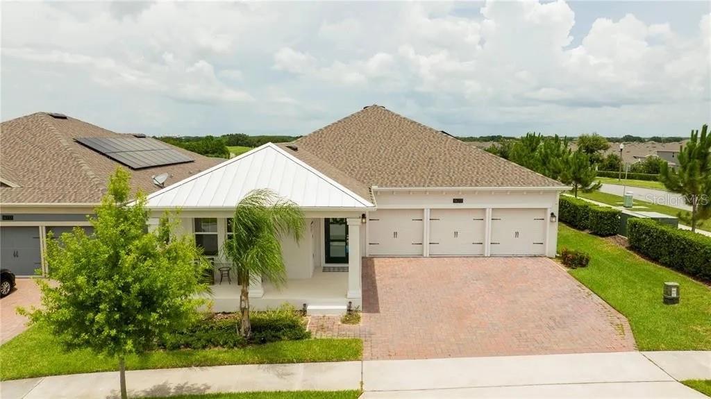 A single-story house with a white metal roof, three-car garage, and a brick paver driveway — 14711 WINTER STAY DRIVE, WINTER GARDEN, FL
