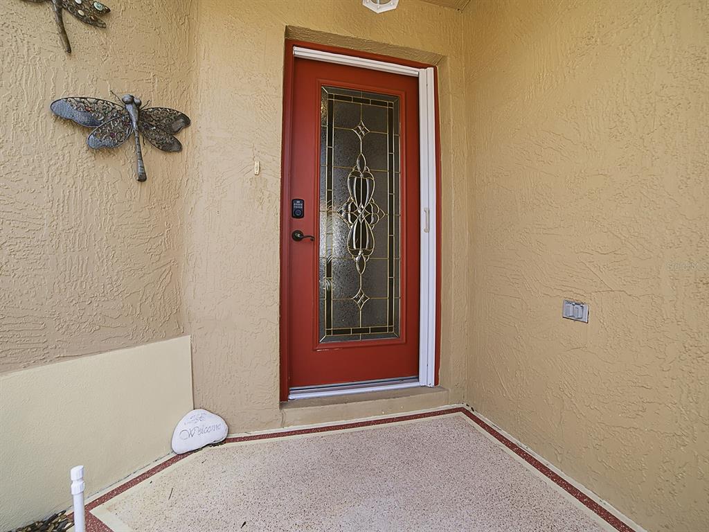 A red front door with a decorative glass insert sits on a covered porch — 7631 SE 170TH LONGVIEW LANE, THE VILLAGES, FL