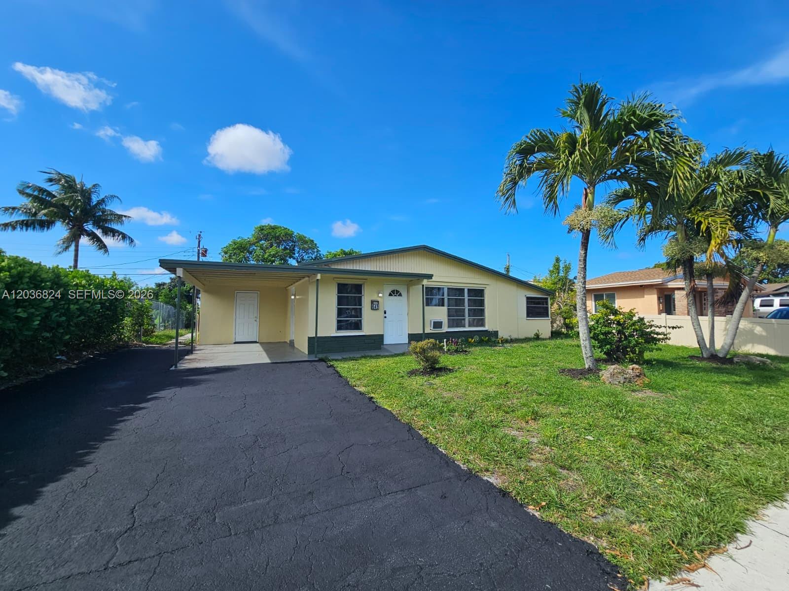 A single-story yellow house features a carport, a black asphalt driveway, and palm trees — 649 NW 19th St, Pompano Beach FL 33060, POMPANO BEACH, FL