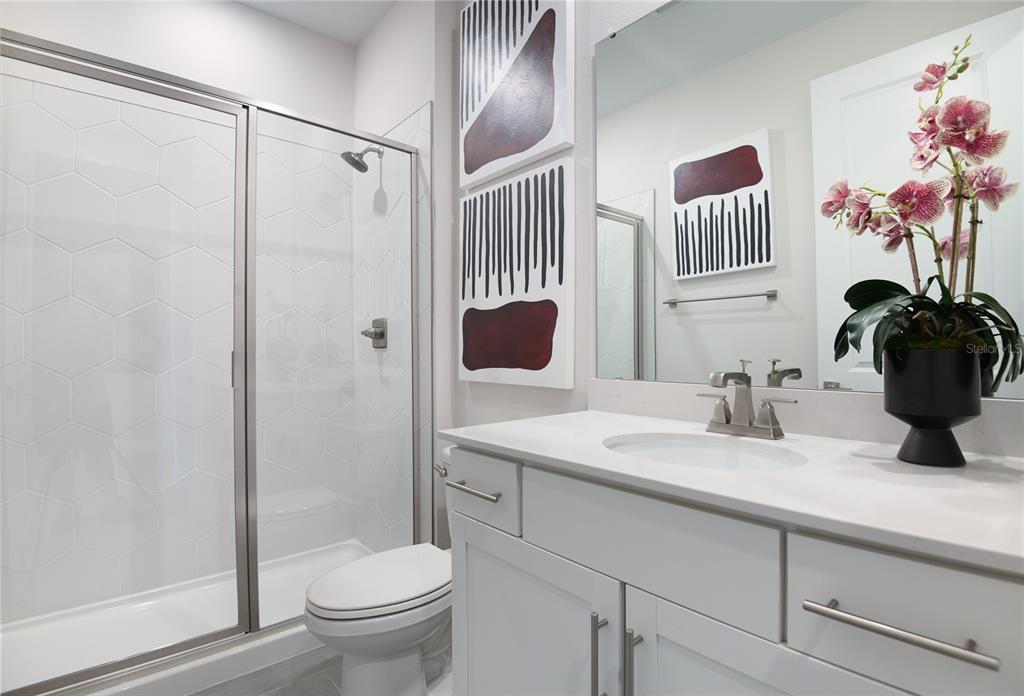 A bathroom features a glass-enclosed shower, a white vanity with a sink, and wall art — 10152 TURNBERRY LANE, LEESBURG, FL