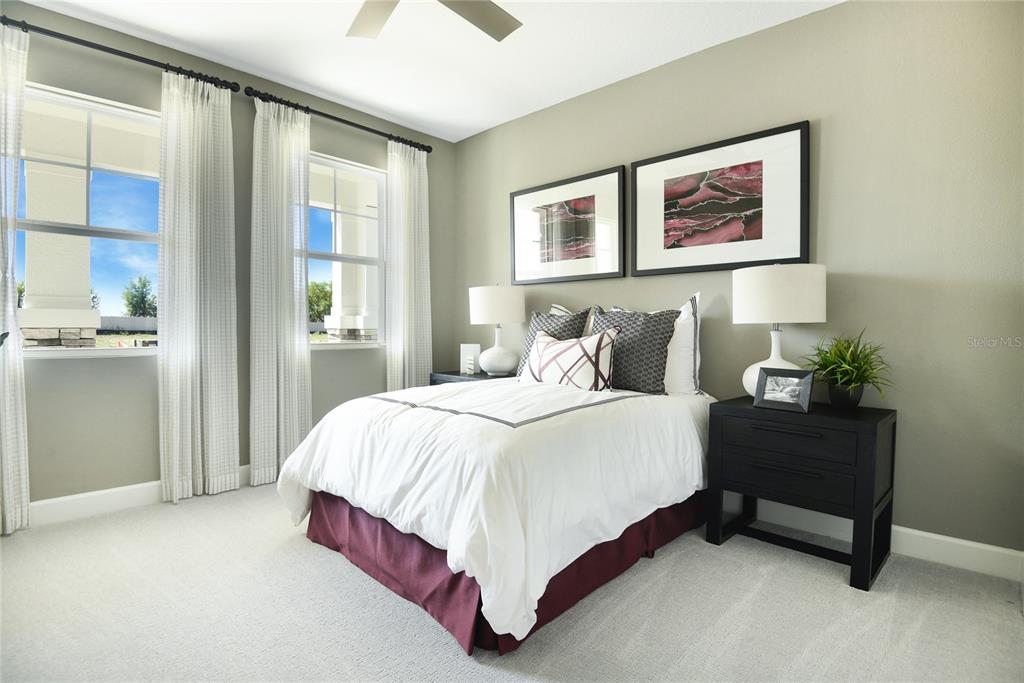 A bedroom features a bed with a maroon skirt, two nightstands, and two framed wall prints — 10152 TURNBERRY LANE, LEESBURG, FL