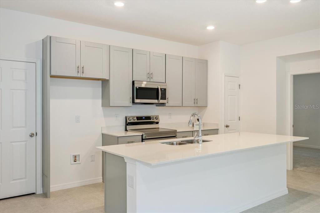 A kitchen features gray cabinets, stainless steel appliances, and a white quartz island countertop — 1202 ATLANTIC AVENUE, FRUITLAND PARK, FL