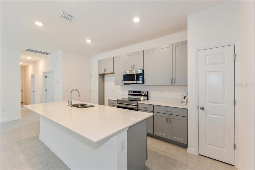 A modern kitchen features a white island, gray cabinets, stainless steel appliances, and tile flooring — 1202 ATLANTIC AVENUE, FRUITLAND PARK, FL