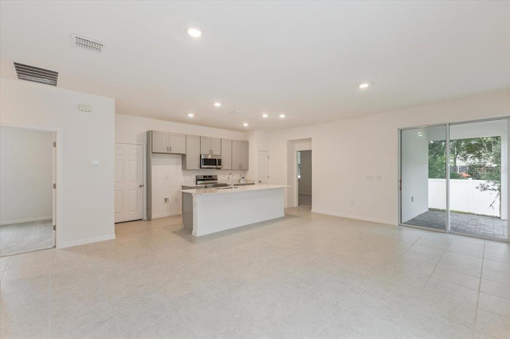 An open-concept kitchen with gray cabinets and a white island overlooks a tiled living area — 1202 ATLANTIC AVENUE, FRUITLAND PARK, FL
