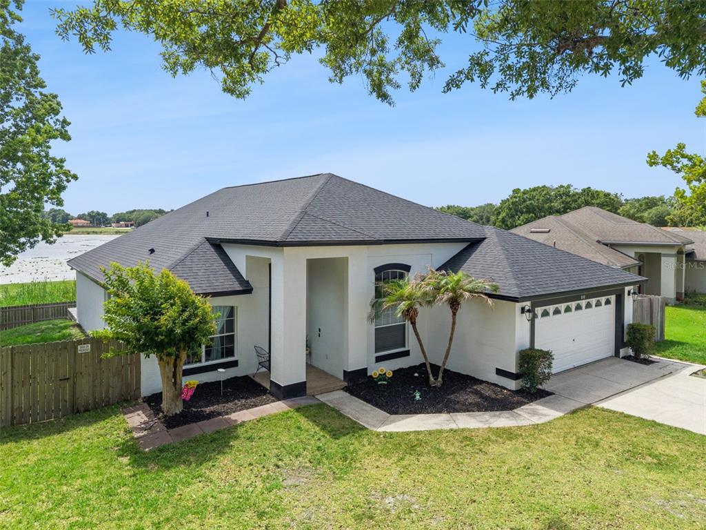 A single-story white house with a dark roof and a two-car garage sits lakeside — 808 LAKE JACKSON CIRCLE, APOPKA, FL