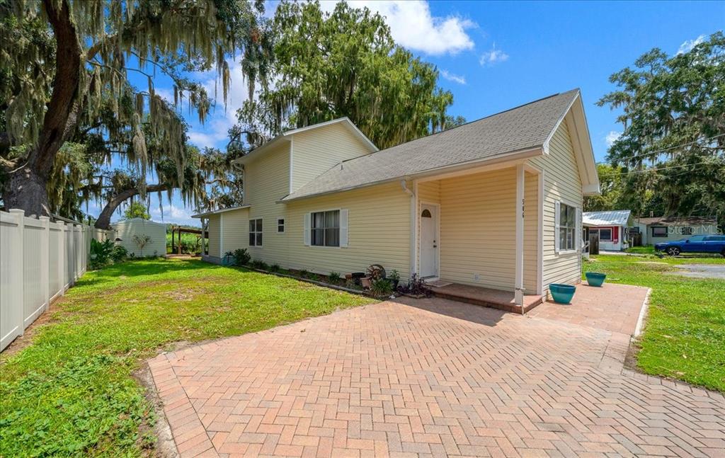 A yellow two-story house with a brick paver driveway and a white vinyl fence — 506 LAKE STREET, INVERNESS, FL