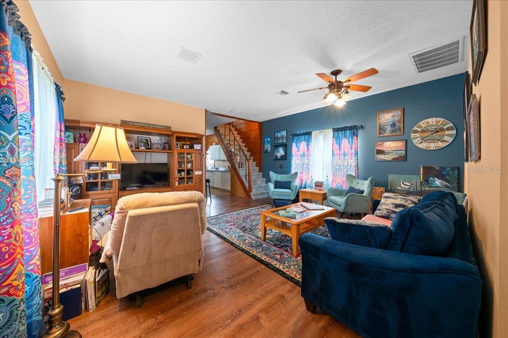 A living room features a blue accent wall, wood flooring, a staircase, and patterned curtains — 506 LAKE STREET, INVERNESS, FL