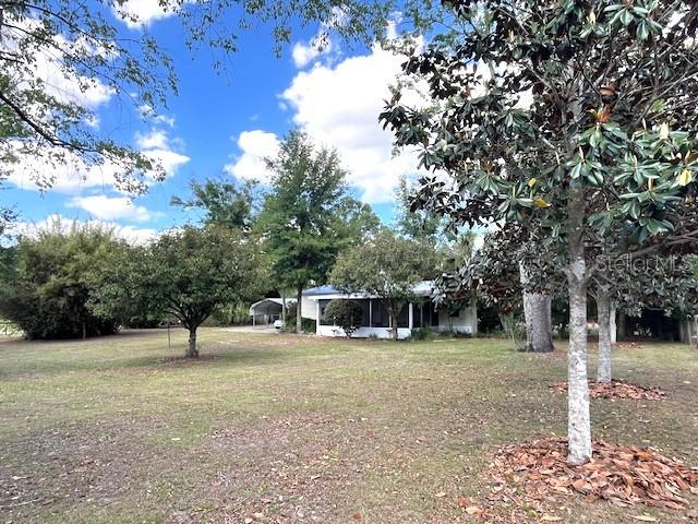 A white house with a screened porch sits on a large, grassy, tree-filled lot — 1569 NW 109TH AVENUE, OCALA, FL