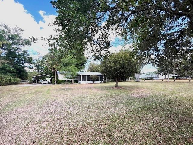 A single-story house with a carport sits on a large, tree-shaded grassy lot — 1569 NW 109TH AVENUE, OCALA, FL