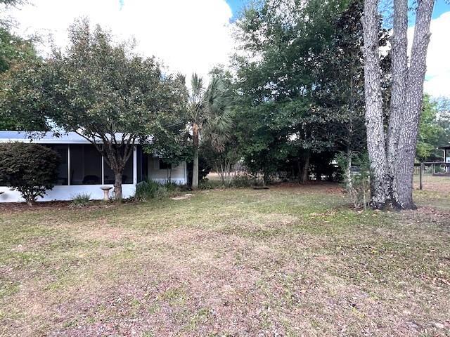 A view of a house exterior with a screened porch, trees, and a grassy yard — 1569 NW 109TH AVENUE, OCALA, FL